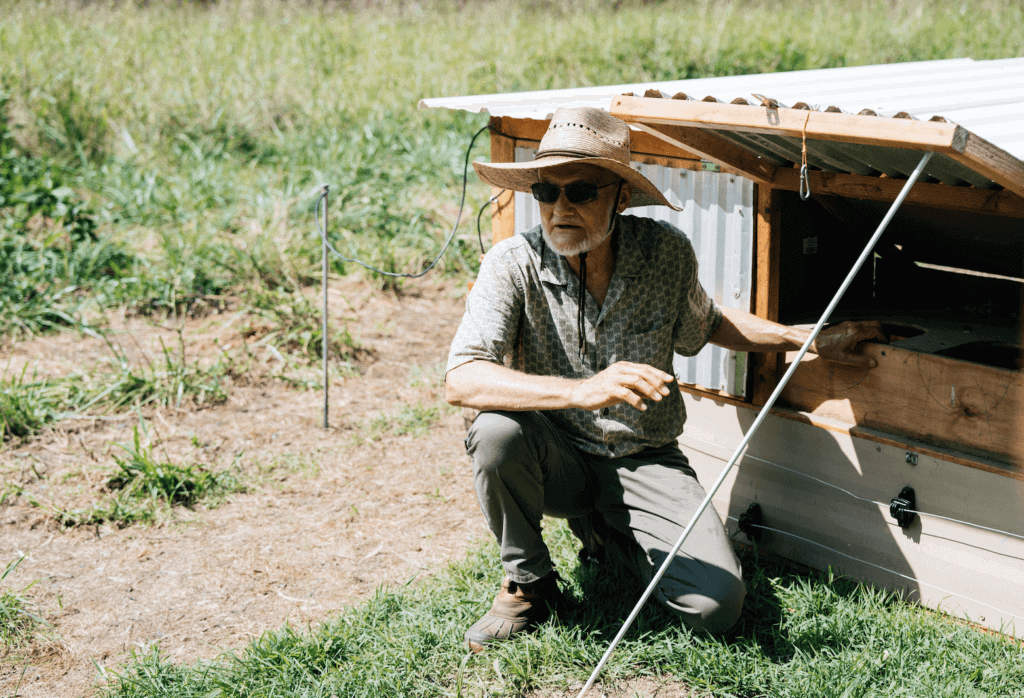 A man crouched by a portable chicken coop.