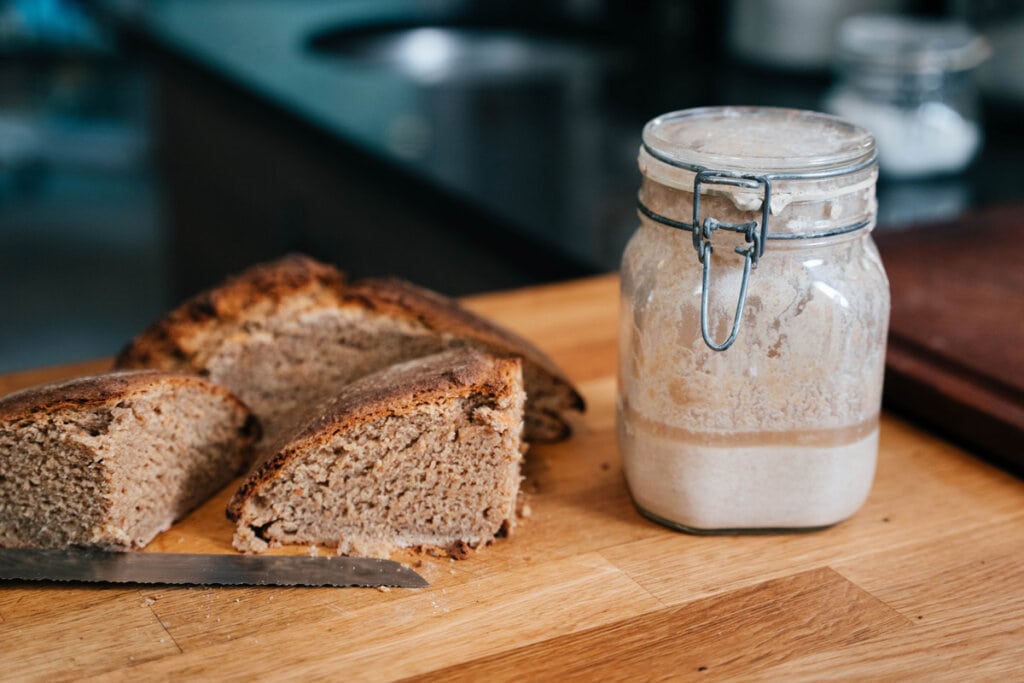 A loaf of sourdough bread next to a jar of sourdough starter.