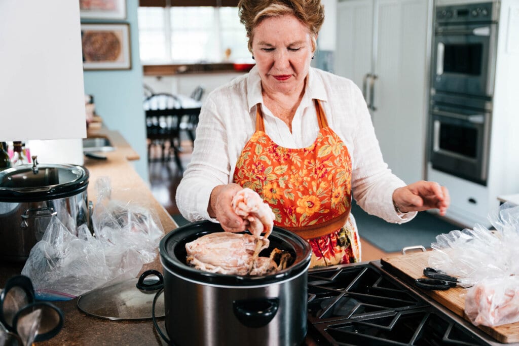 A woman adding ingredients for bone broth to a crockpot.