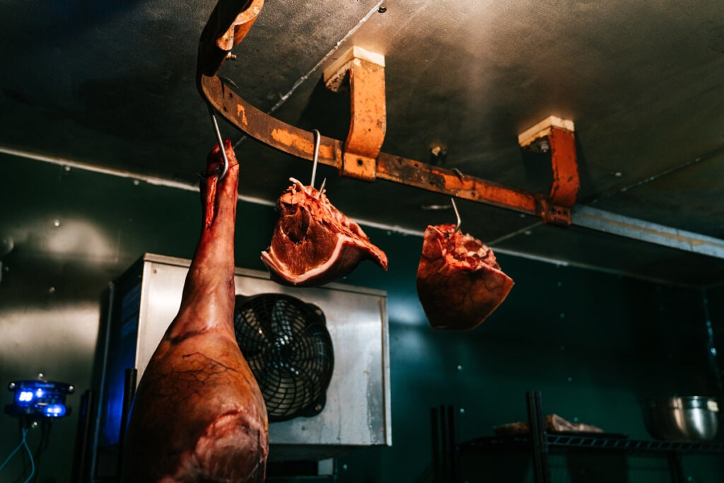 Cured meat hanging from a refrigerator ceiling.