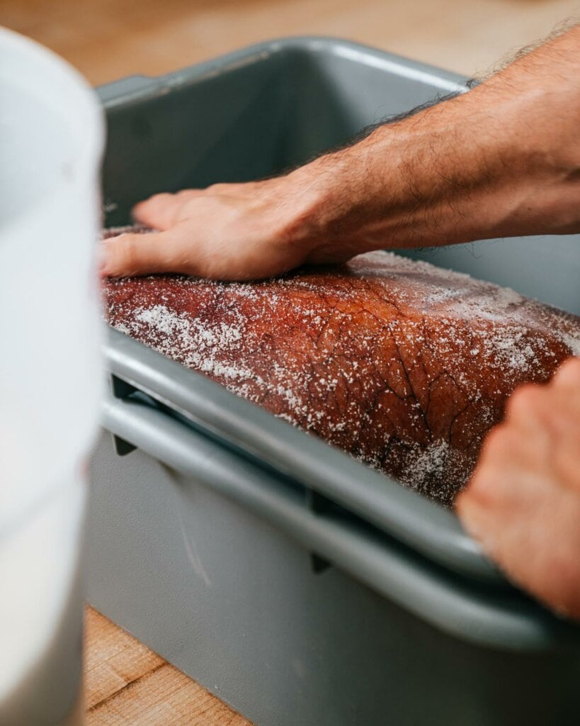 A large piece of meat being rubbed with salt for curing.