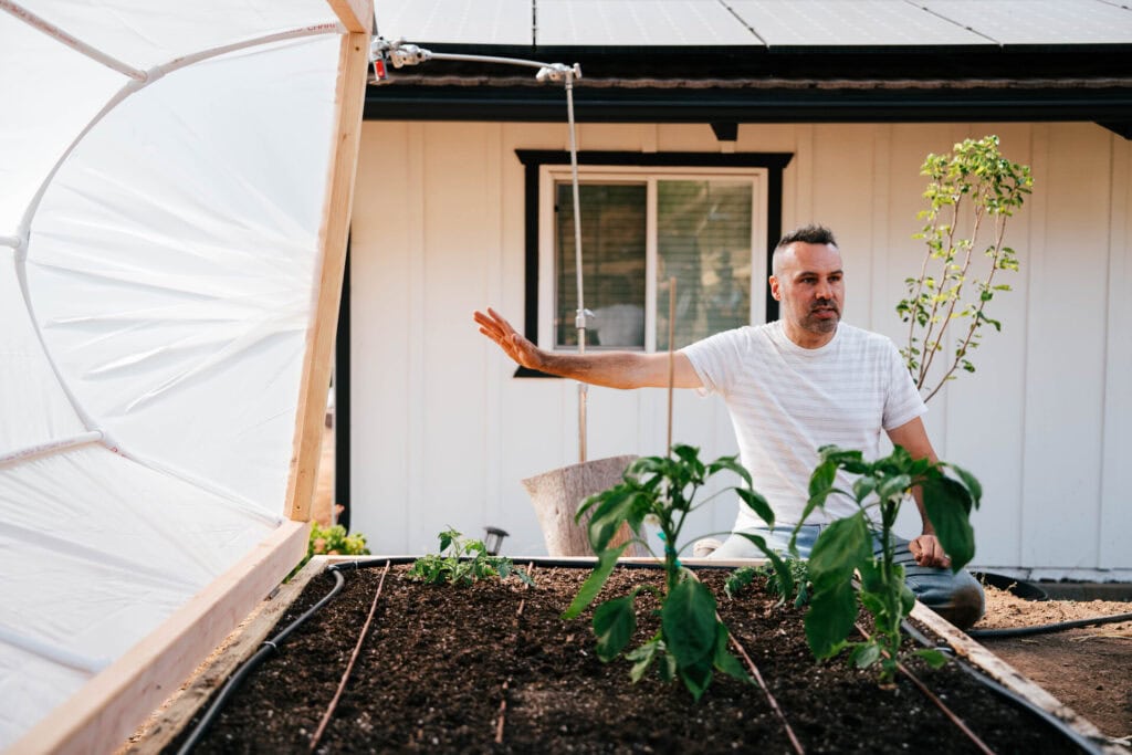 Brian Lowell kneeling beside a raised bed and mini hoop house, explaining how seasonal protection helps extend the growing season