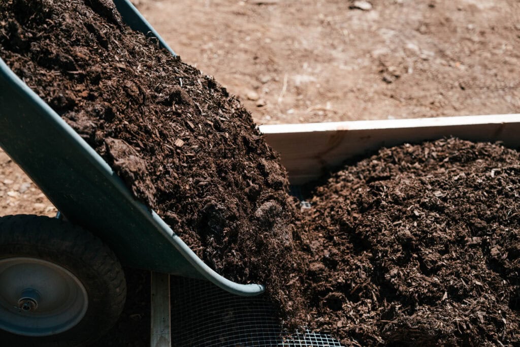 Wheelbarrow dumping compost-rich soil mix into a newly built raised garden bed