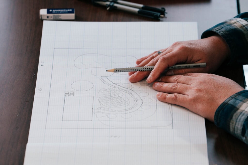 Hands sketching a garden layout on graph paper while planning planting beds and crop placement for the coming season.