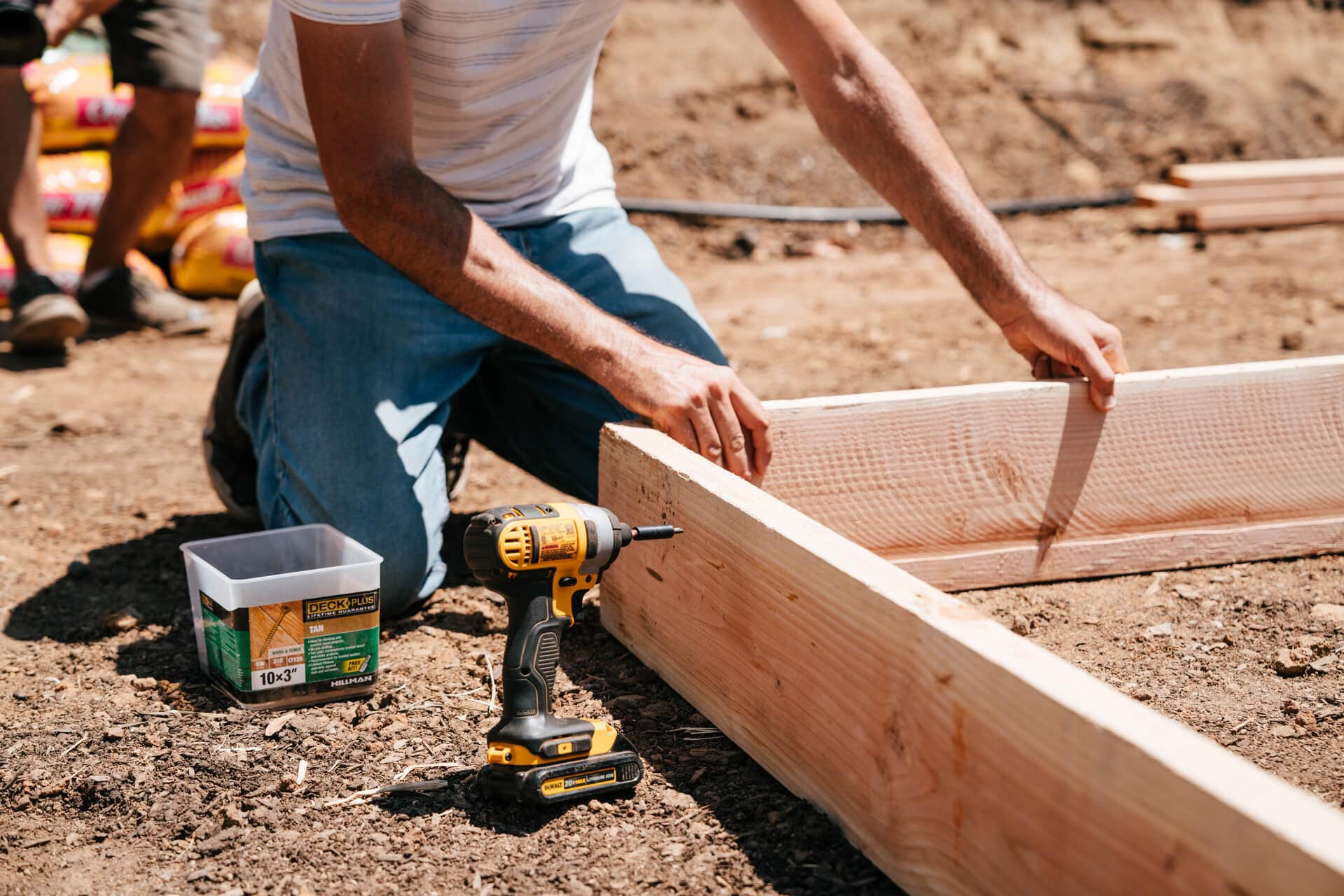 Gardener assembling a wooden raised garden bed with a drill and deck screws