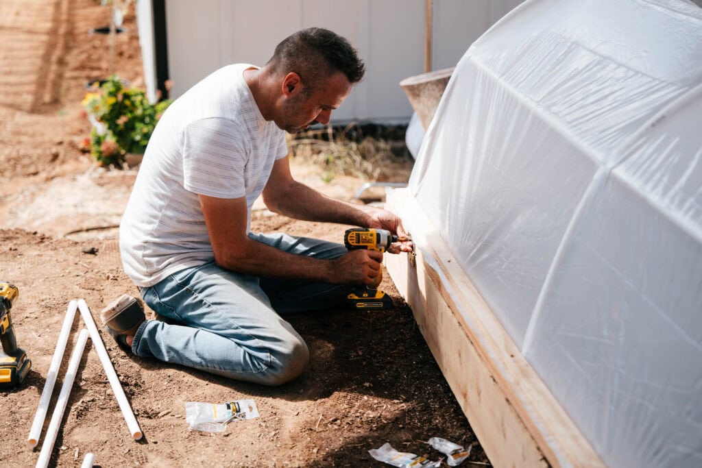 Brian Lowell attaching plastic covering to a raised bed hoop house for frost protection in a short-season or cold-climate garden