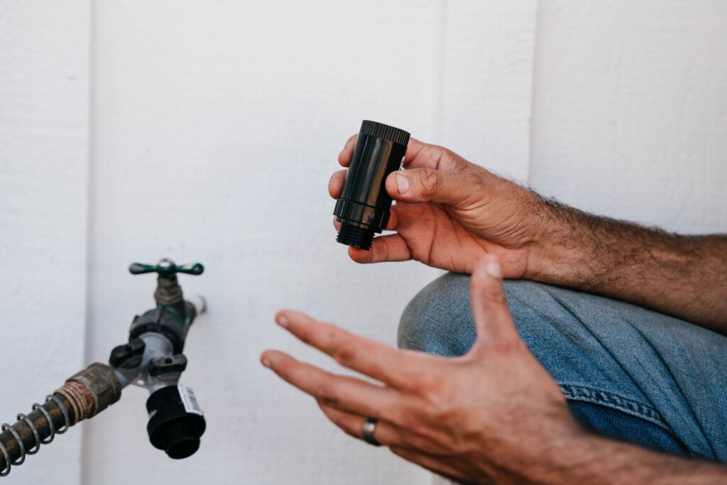 Hand holding drip irrigation connector near outdoor water spigot