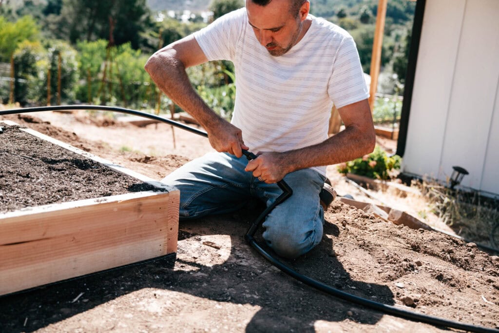 Person connecting drip irrigation tubing to a raised garden bed system