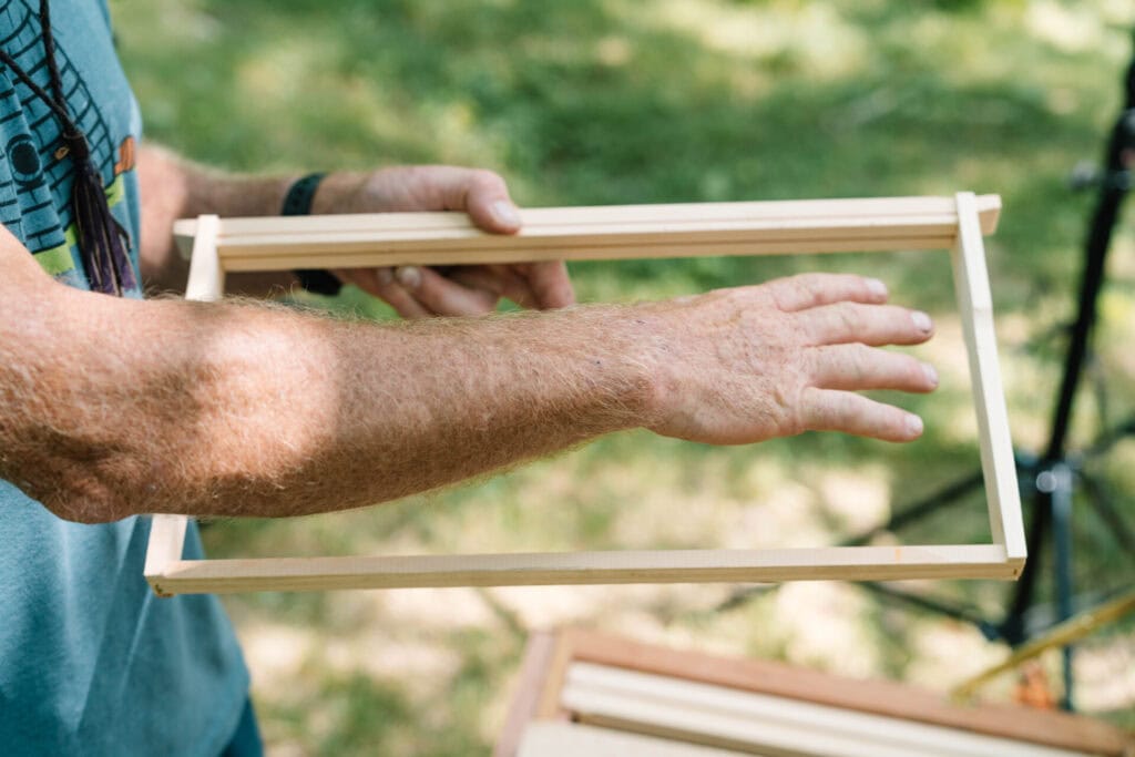 Close-up of hands showing spacing and placement on a wooden swarm trap frame
